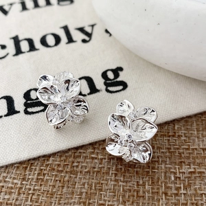 Three-petal silver flower stud earrings with micro-set zircons on textured canvas background