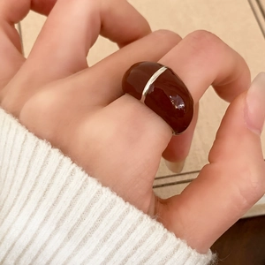 Retro deep red resin ring with silver metal lines worn by a model on a beige surface