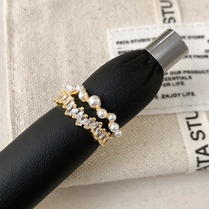 Double layered gold ring with elegant white pearls and baguette-cut zircons on a black stand
