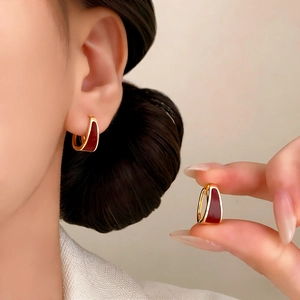 U-shaped gold earrings with deep red enamel inlay shown on hand in a minimalist style