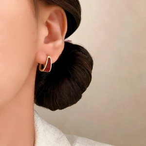 Elegant U-shaped gold earrings with deep red enamel inlay worn by a female model