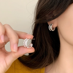 Silver beaded C-shaped hoop earrings with woven texture worn by a model in soft light