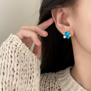 Elegante gouden oorbellen met blauwe vierkante kristallen en witte parel bij een model