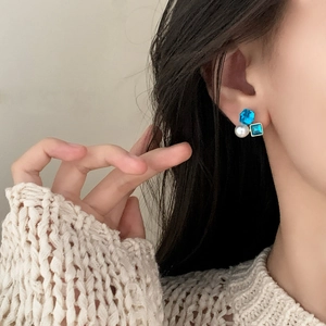 Elegante gouden oorbellen met blauwe zirkoon en witte parel op een model