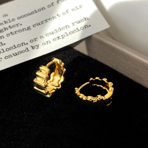 Macro shot of gold-plated hoop earrings featuring textured wavy patterns and metallic luster