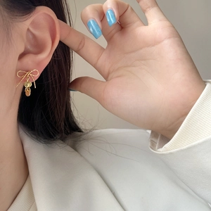 Elegant gold bow earrings with three dangling metal discs worn on a female model