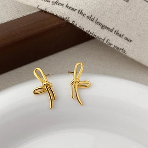 Detailed close-up of golden bow-shaped stud earrings on a vintage ceramic plate