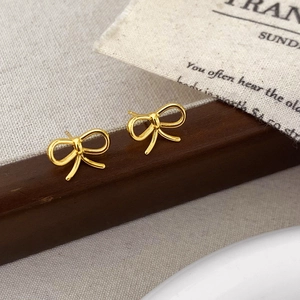 Macro shot of polished gold bow stud earrings on a dark wood and fabric background