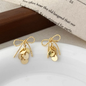 Detail of golden bow earrings with shimmering round metal sequins on a white ceramic plate
