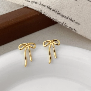 Detailed view of elegant gold bow stud earrings on a white porcelain plate decor