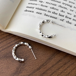 Minimalist silver C-shaped earrings with faceted geometric surface on book background