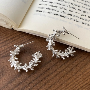 Detail shot of silver branch texture C-shaped earrings on a rustic wood background