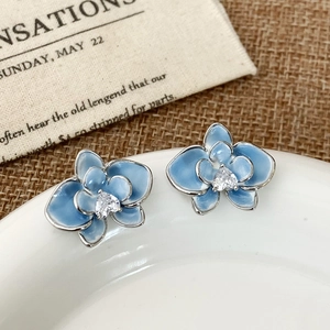 Close-up of blue enamel orchid stud earrings with crystal center on a ceramic plate