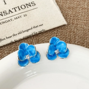 Macro detail of blue floral enamel earrings with central zircon on white porcelain