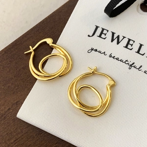 Macro view of minimalist layered gold hoop earrings with twisted design on white card
