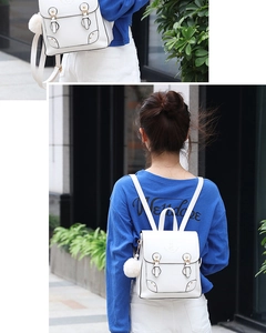 Close-up of white leather mini backpack with decorative buckles and fuzzy pom-pom charm