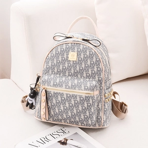 Chic mini cream backpack with grey letters, gold rivets and cute bear pendant on a sofa