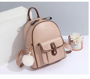 Détail du sac à dos beige en similicuir avec bordure marron et breloque pompon blanc