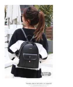 Vue arrière d'un petit sac à dos en similicuir noir avec pompon blanc porté par un mannequin
