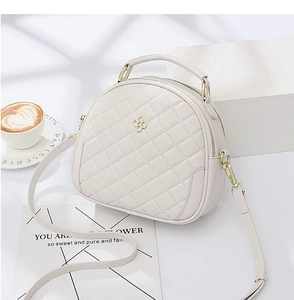 Close-up of beige quilted half-round bag with gold clover logo and metallic hardware