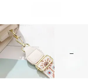 Gros plan détaillé de la boucle dorée et de la bandoulière brodée sur un sac blanc pur