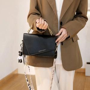 Borsa a tracolla chic in pelle nera con catena d'oro, cuciture e ciondolo a orso