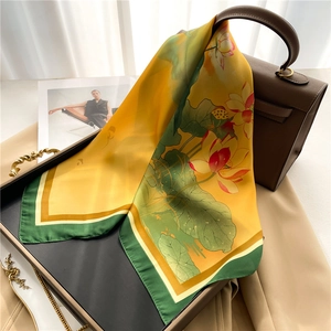 Elegant lotus floral silk scarf in yellow and green draped over a stylish handbag