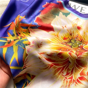 Macro detail showing vibrant lotus flower print and silky texture on purple square scarf