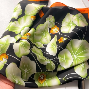 Detail of silk scarf showing floral print and vibrant orange border on black satin fabric