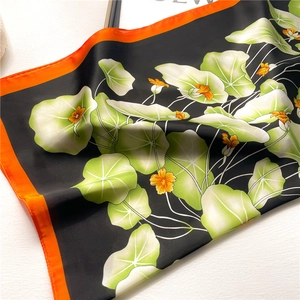 Detailed macro view of the glossy lotus leaf pattern and orange hem on silk scarf