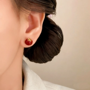 Elegant red enamel stud earrings with gold bow accents worn by a stylish model