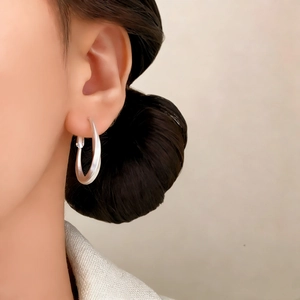 Minimalist matte silver oval twist earrings shown in a close-up profile view on a model