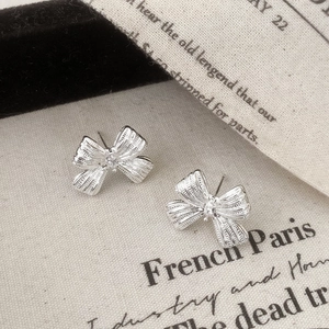 Detail of silver bow earrings with micro zircon stone and textured metal surface