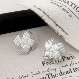 Macro detail of silver windmill stud earrings with intricate woven texture on linen