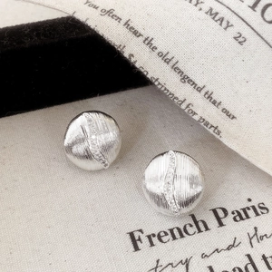Detailed view of silver stud earrings with radial texture and wavy zircon inlay