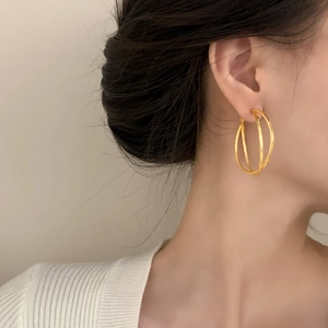 Elegant triple-layered gold geometric hoop earrings worn by a model in a minimalist setting