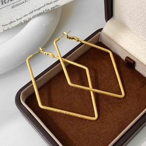 Macro shot of large golden geometric rhombus earrings with a frosted matte finish