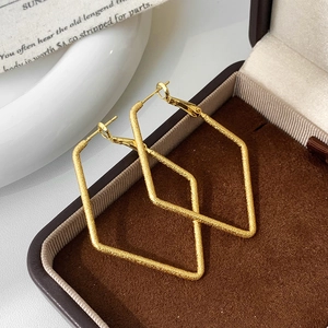 Macro detail of geometric rhombus hoop earrings with a matte frosted gold finish