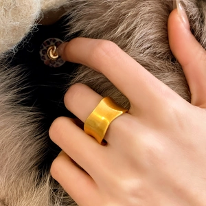 Close-up of a wide gold ring with matte brushed finish and irregular wavy edges