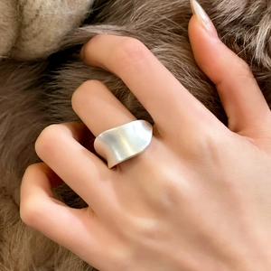 Modern minimalist silver brushed metal ring with asymmetric streamlined design worn on hand