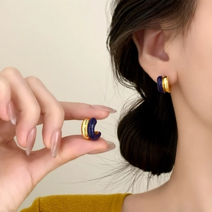 Modern gold-plated C-shaped hoop earrings with navy blue enamel inlay on a model