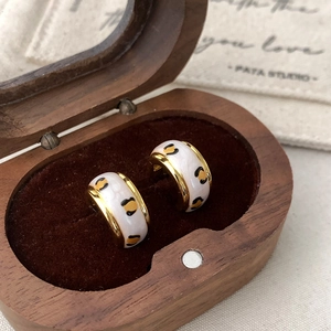 Macro detail of leopard print enamel hoop earrings on velvet padding in wooden box