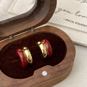 Detail of red enamel and gold C-shaped earrings on a premium wooden jewelry box