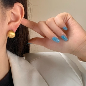 Detail of matte gold half-sphere earrings with brushed texture on model in white blazer
