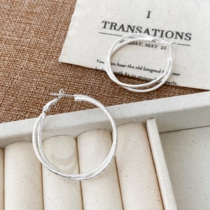 Close-up of silver geometric double-hoop earrings with a fine matte sandblasted finish