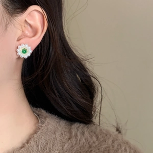 Detail of flower-shaped pearl earring with green gemstone worn on model's ear