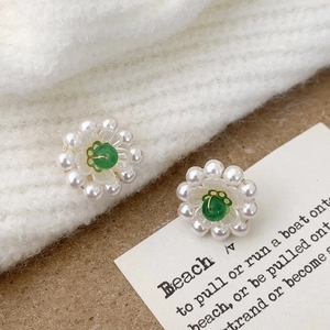 Detail of flower stud earrings featuring green stone center and white pearl petals