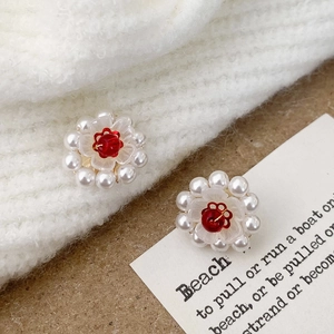 Detailed close-up of handmade floral earrings with white pearls and red beads on fabric
