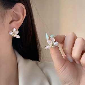 Dettaglio di eleganti orecchini a fiore in smalto con petali perlati e bordi in metallo