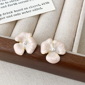 Primo piano di orecchini a fiore in smalto con perle su un vassoio di velluto beige